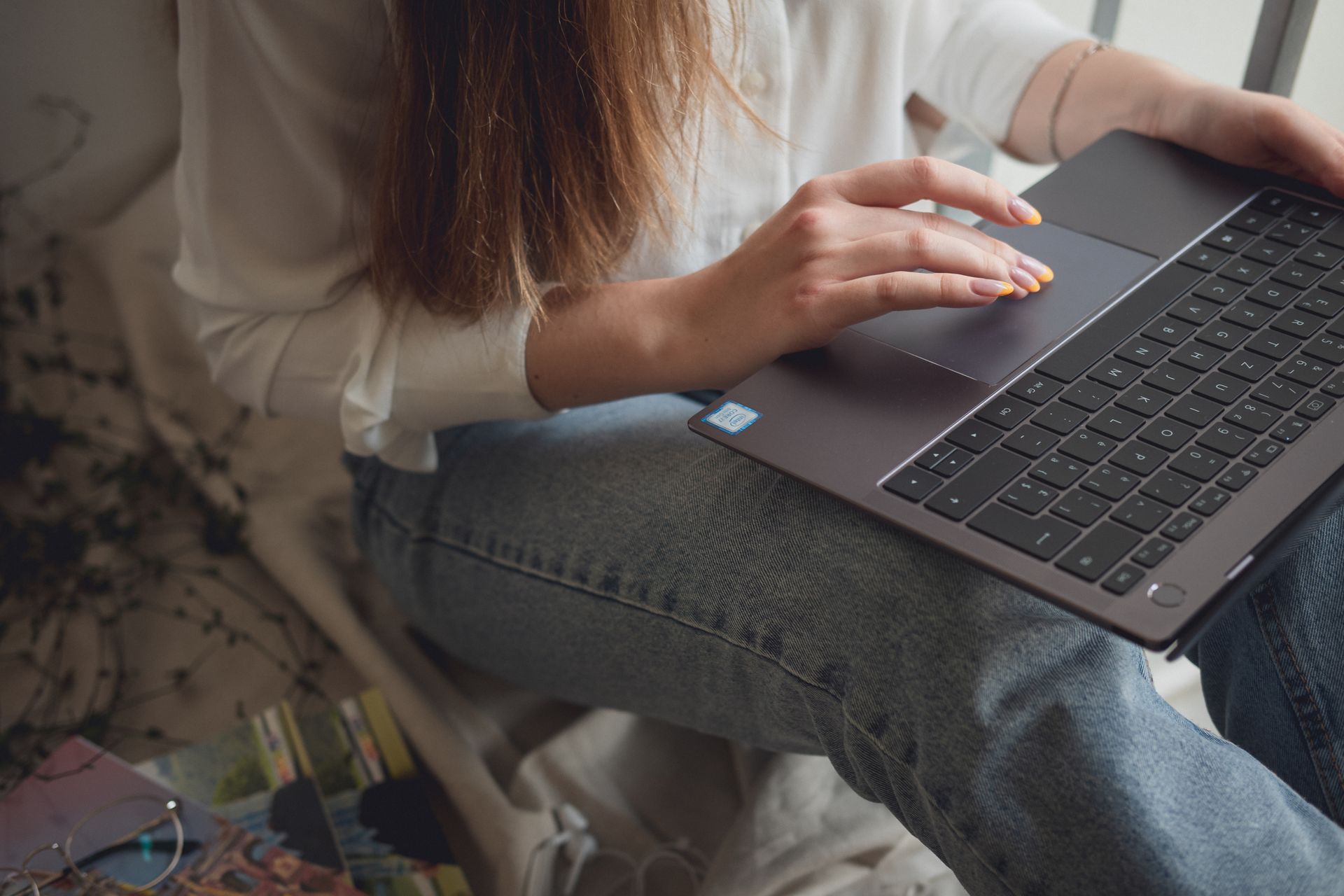 A woman in casual attire working on a laptop at home for study or freelance work.