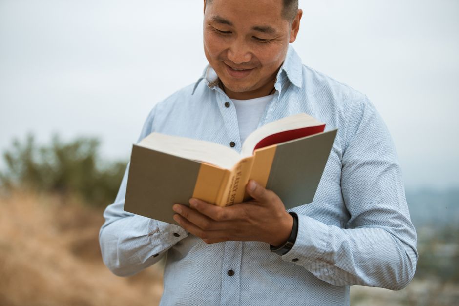 A man enjoys reading a book outdoors on a warm summer day in a scenic field. A man enjoys reading a book outdoors on a warm summer day in a scenic field.