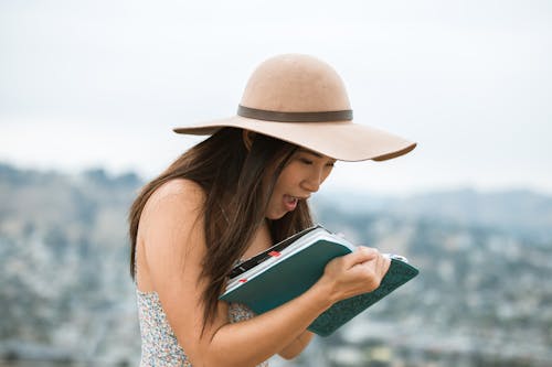 Frau Im Weißen Und Blauen ärmellosen Blumenkleid, Das Braunen Sonnenhut Hält, Der Weißes Ipad Während Hält