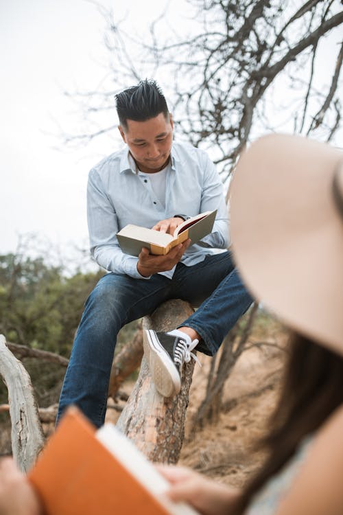 Free Man in Light Blue Long Sleeve Shirt and Blue Denim Jeans Sitting on Brown Tree Branch Stock Photo