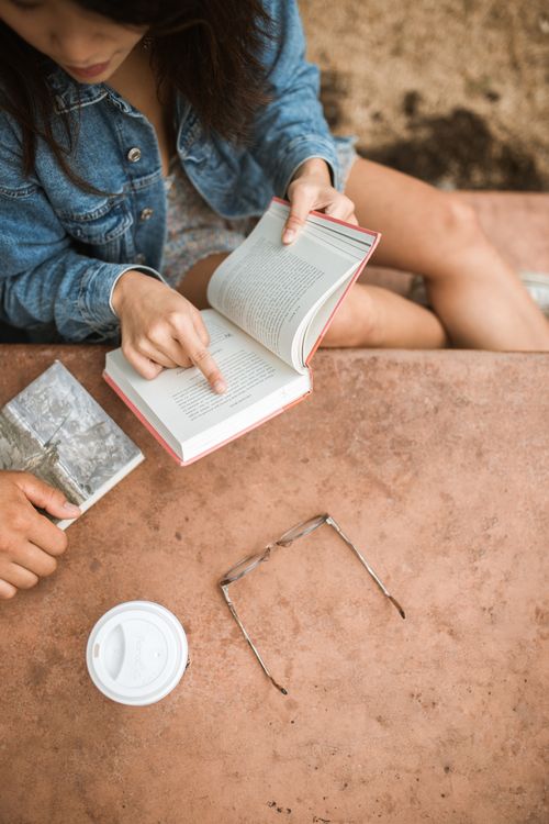 Free A couple enjoys reading books together at an outdoor table, creating a peaceful and educational vibe. Stock Photo