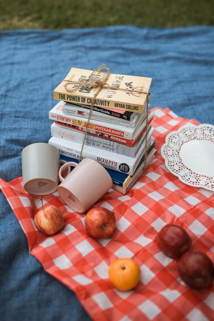 A Stack Of Books And Fruits On A Picnic Blanket