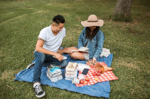 Free A couple reading together during a summer picnic at a park, surrounded by books and snacks. Stock Photo