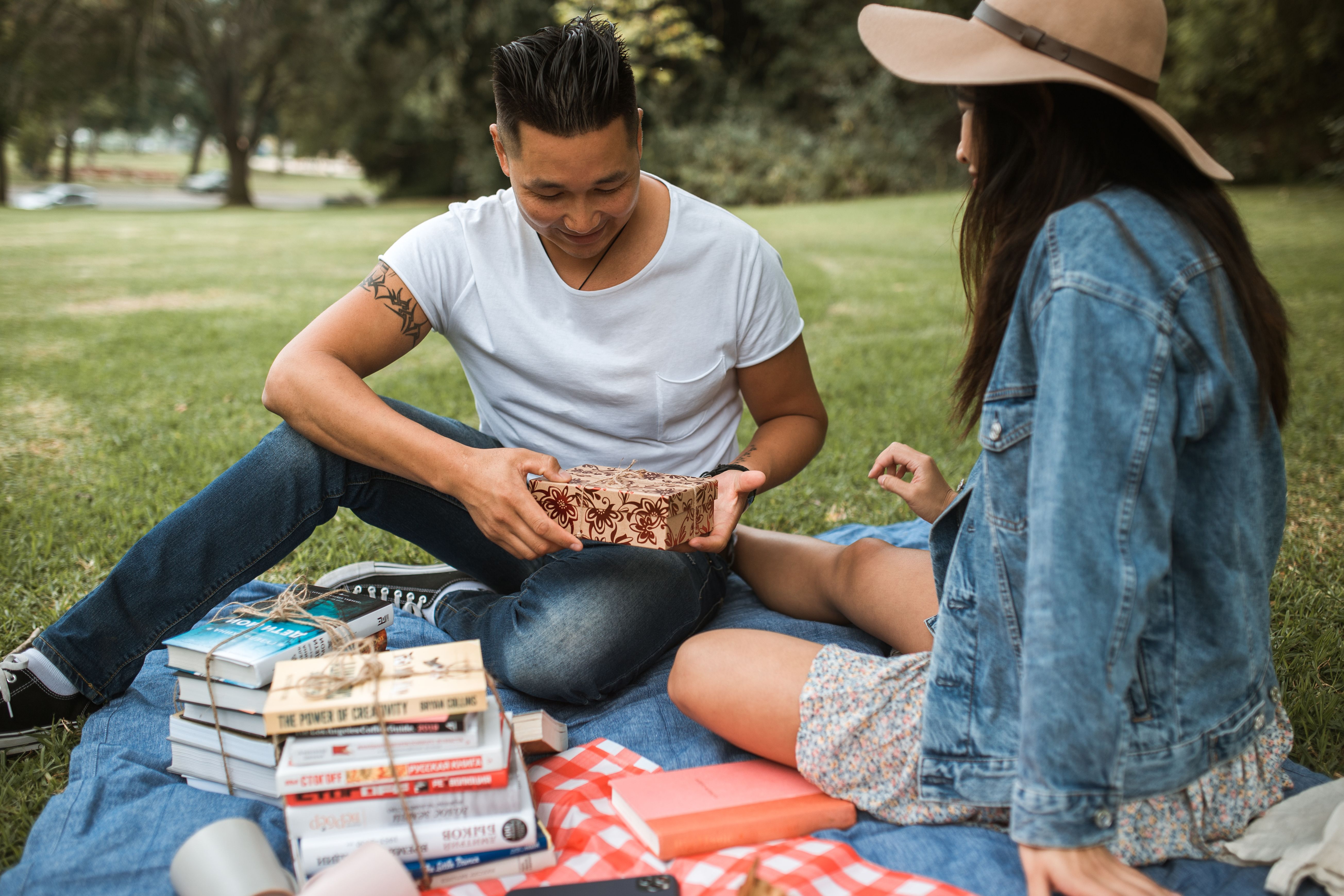 A couple enjoys a sunny picnic, exchanging gifts and relishing leisure time outdoors.