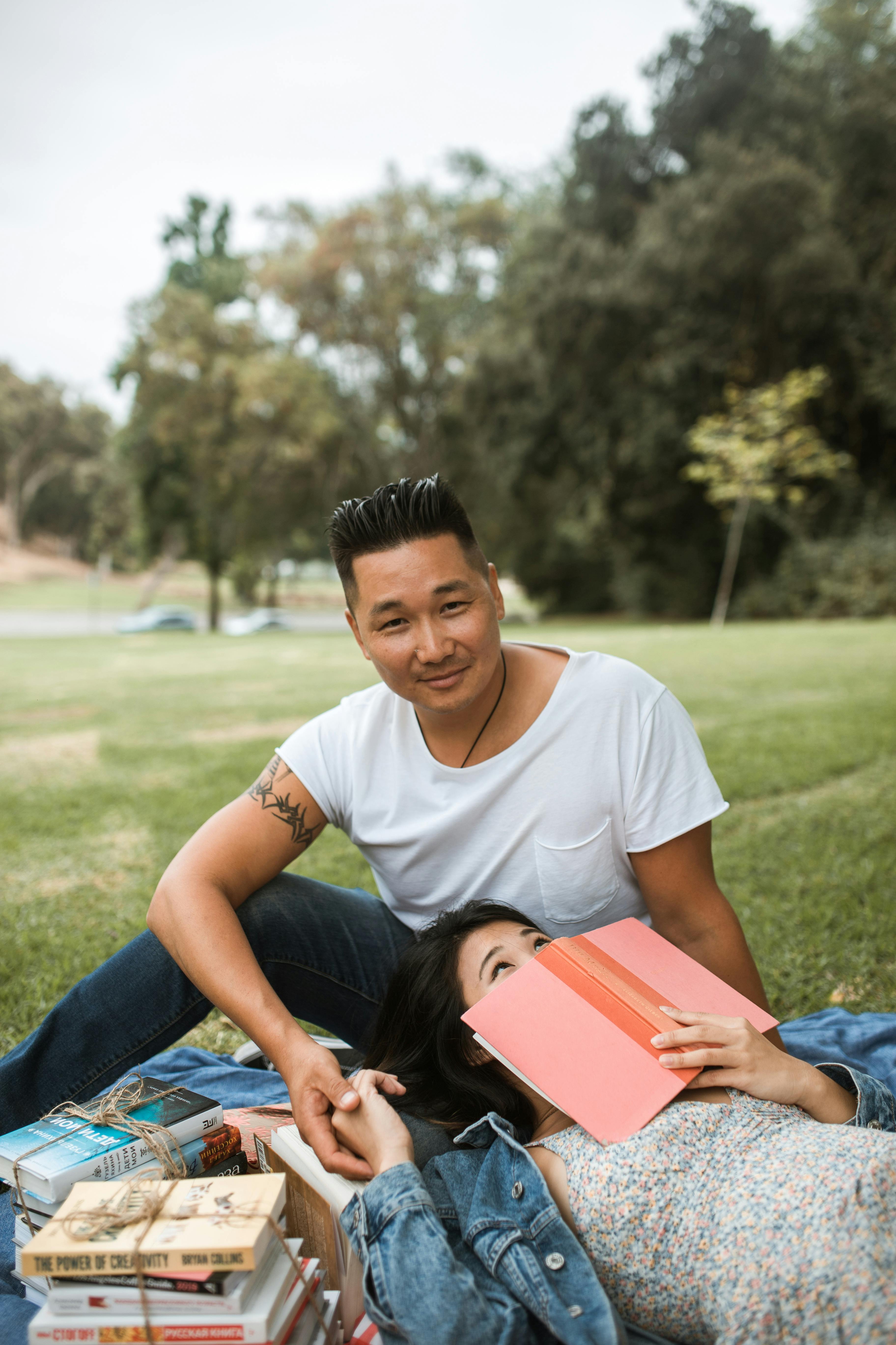 A casual outdoor scene of a couple enjoying a picnic with books on a sunny day in the park.
