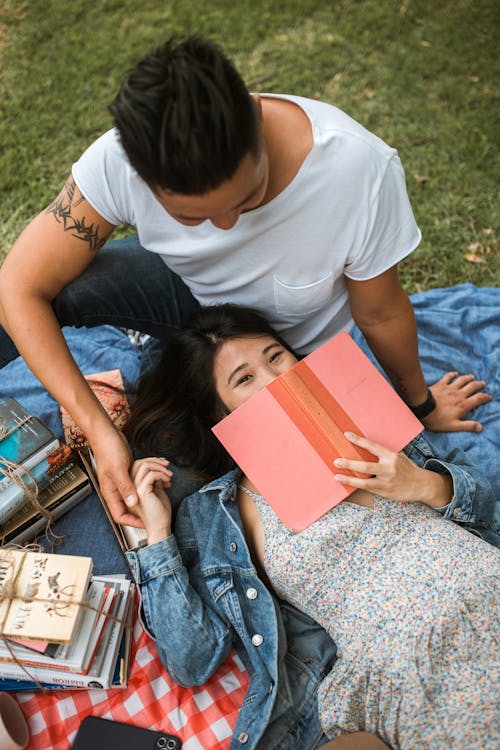 Wanita Dengan T Shirt Putih Dan Jeans Denim Biru Duduk Di Tanah Saat Memegang Buku