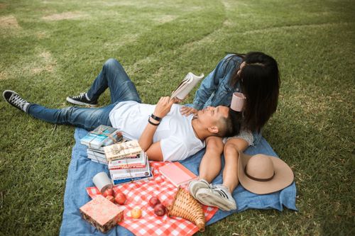 Free A couple lounging on a blanket with books, enjoying a summer picnic in the park. Stock Photo