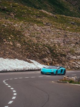 Luxurious blue sports car driving through serene mountain pass.