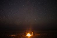 在星光灿烂的天空下，一对夫妇在宁静的海滩上享受篝火，这非常适合夜间摄影主题