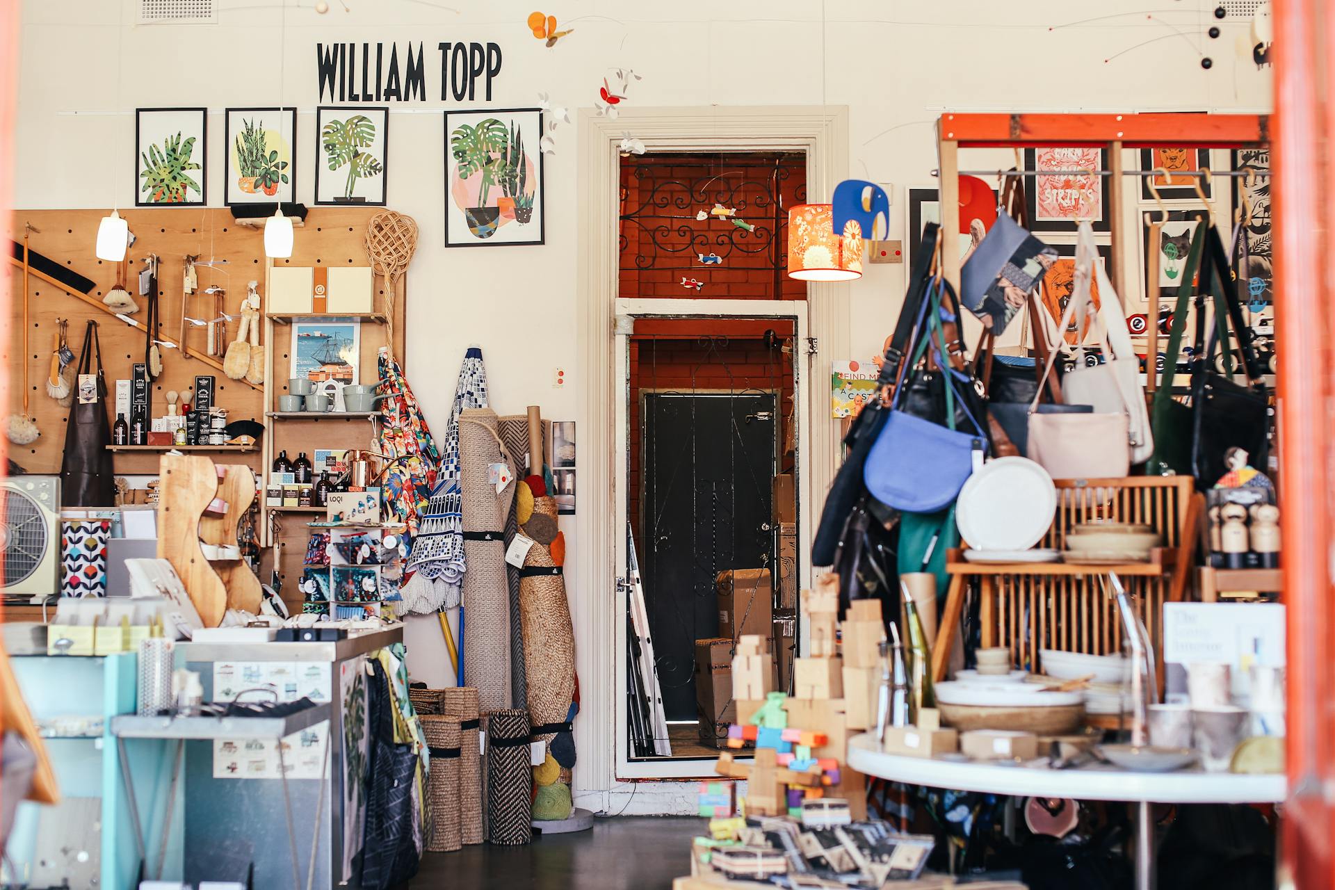 Interior of store with assorted designer goods and abundance of purses hanging on wall near various homewares and modern outfits