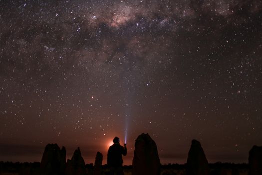 夜晚，一个匿名者的背影坐在大自然中，用手电筒照亮天空中发光的星星