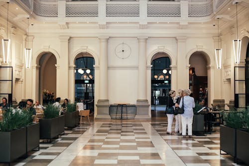 Group of women standing near menu in spacious restaurant with people eating at tables in contemporary hotel with green vegetation