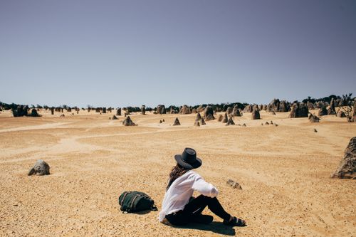 Free A woman sitting and relaxing in a sandy desert surrounded by unique rock formations under a clear sky. Stock Photo