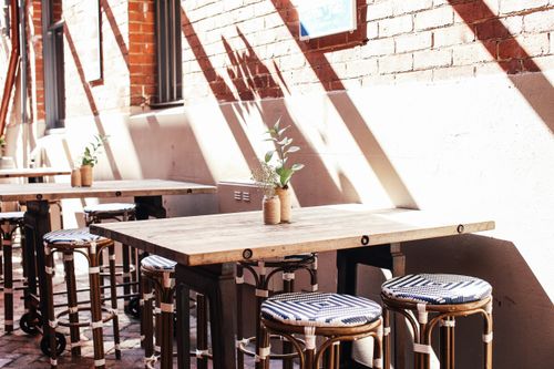 Free Sunlit outdoor cafe featuring rustic tables, stylish stools, and decorative plants. Stock Photo