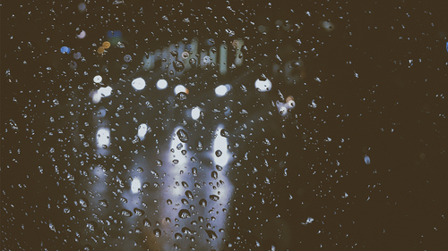 Free Rain droplets on a window with blurred city lights creating a moody atmosphere at night. Stock Photo