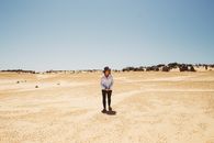 Man in White T-shirt and Black Pants Standing on Brown Sand