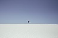 Person in Black Jacket Jumping on White Sand