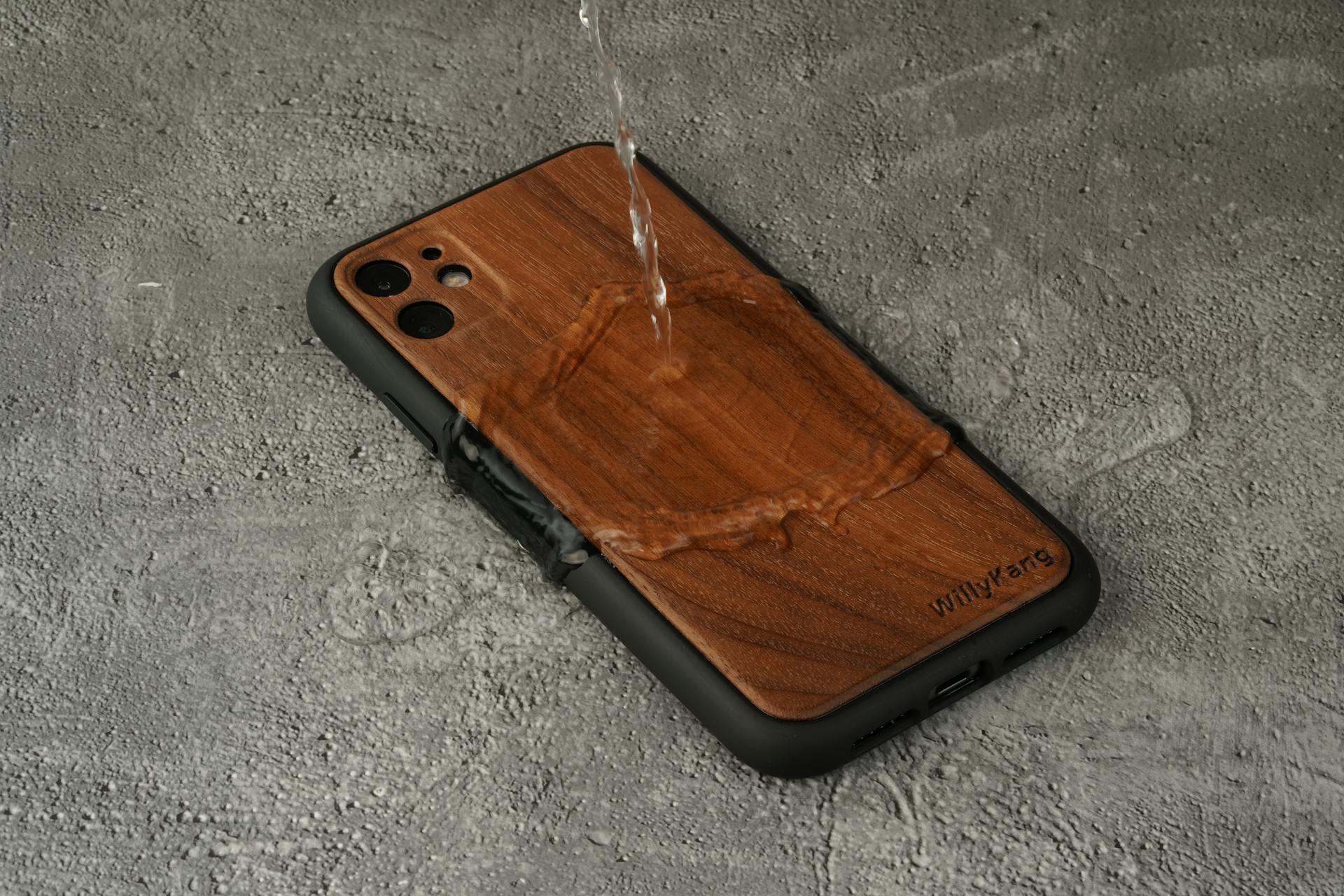 Durable waterproof wooden phone case with water pouring on a concrete background.