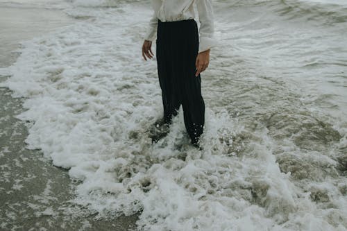 Free A Person in Black Pants Standing on the Shore Stock Photo