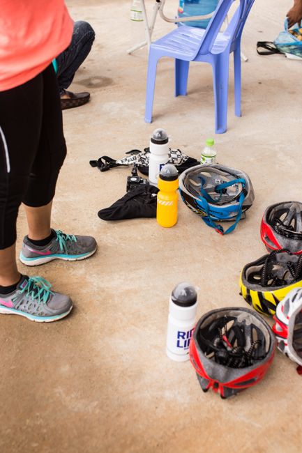 Cycling gear with helmets and water bottles on ground during a break.