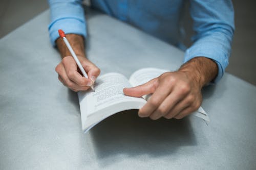 Человек в синей рубашке с длинным рукавом держит ручку и книгу