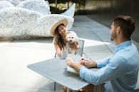 阳光明媚的户外咖啡馆里，一个戴着草帽的女人抱着她的狗，进行了一次友好的会面