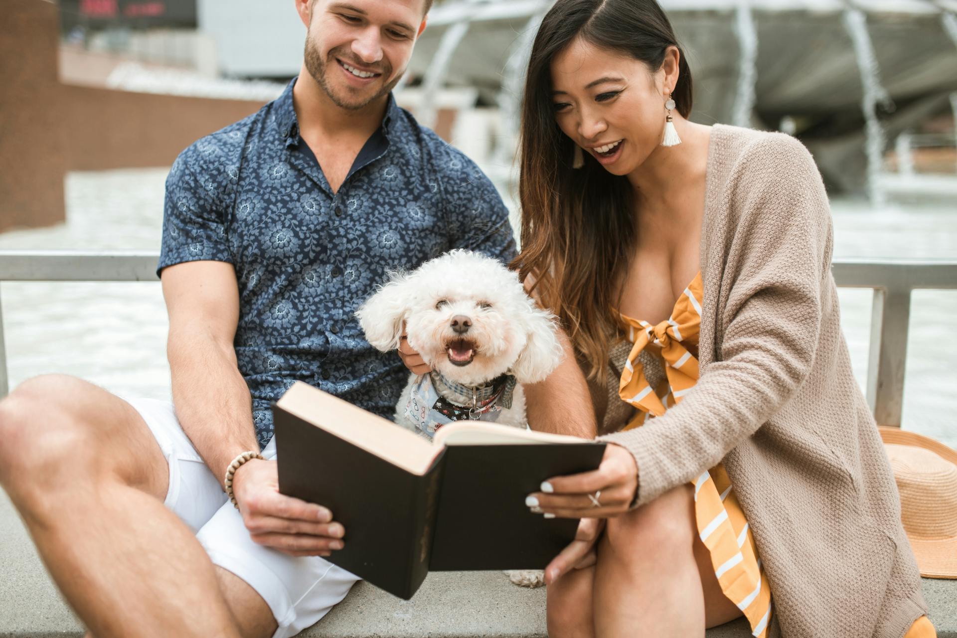 White Dog Sitting Between a Man and a Woman while Reading a Book