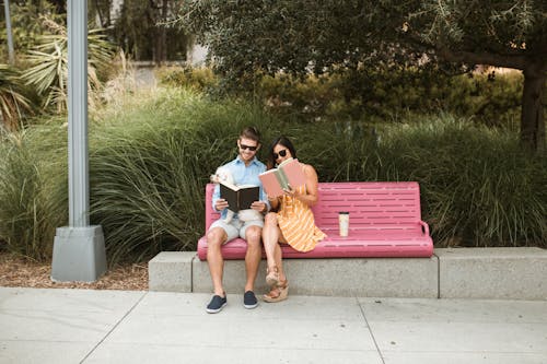 Couple Sitting on Pink Bench Reading Books Together 