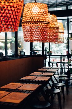 Warmly illuminated restaurant with bamboo lampshades and empty chairs, creating a cozy atmosphere.