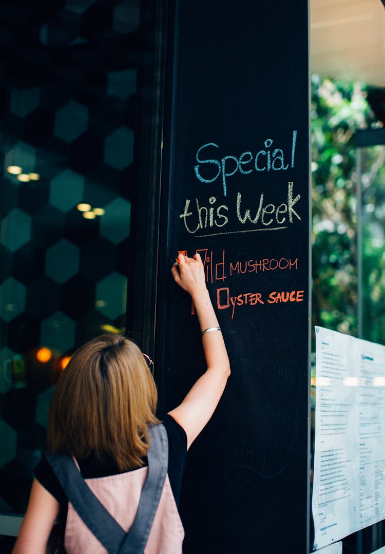 Woman Writing With Chalk On Board In Restaurant 