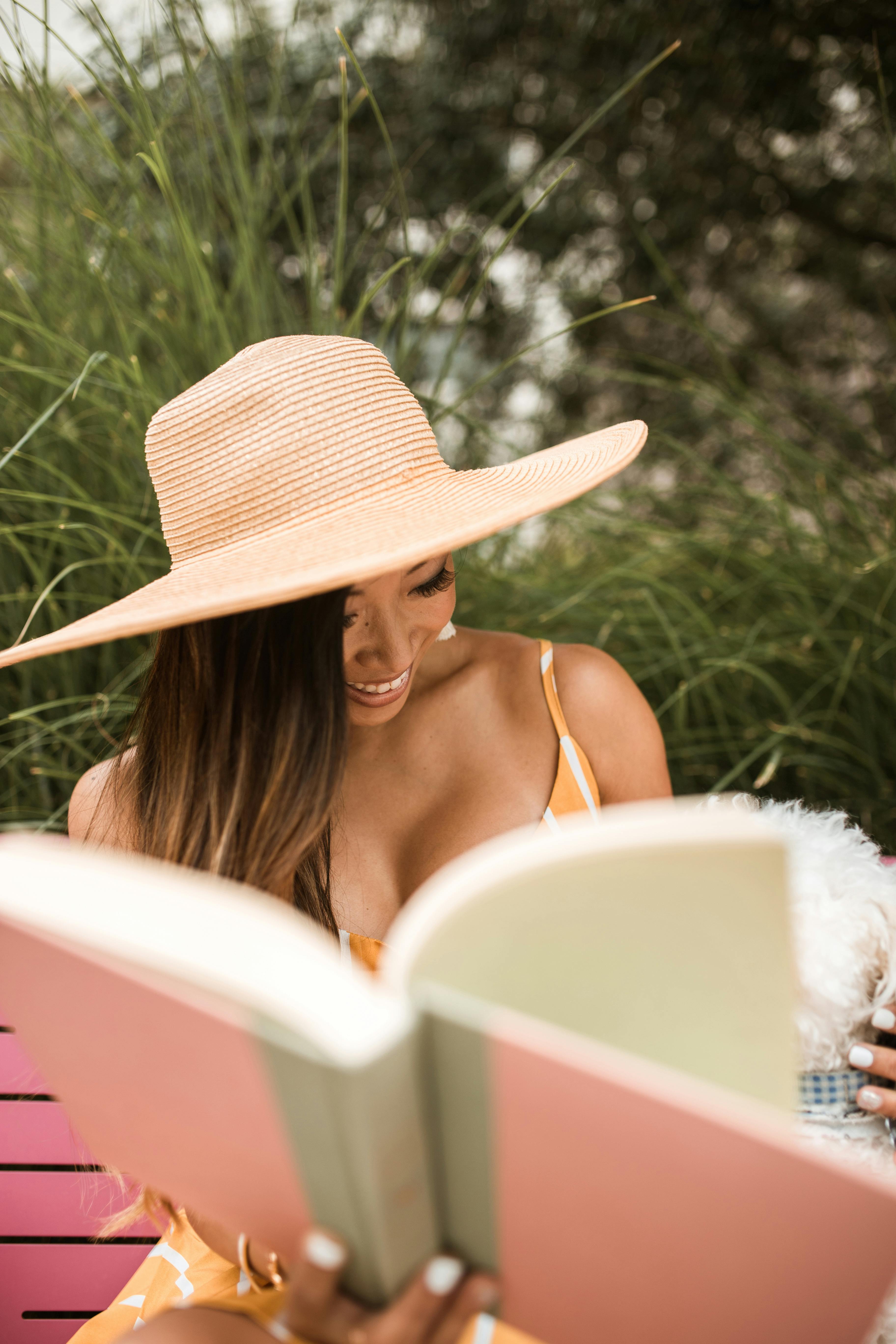 一位微笑的女人喜欢戴着时尚的遮阳帽在阳光下阅读