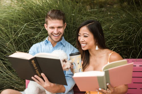 Uomo In Camicia Di Vestito Blu Che Tiene Libro Nero Accanto Alla Donna In Vestito Senza Maniche Bianco