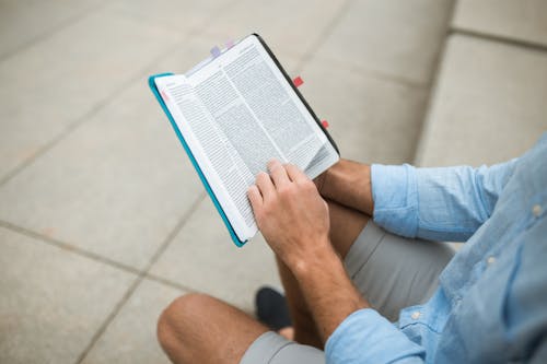 Person in Blue Long Sleeves and Gray Shorts Holding a Bible 