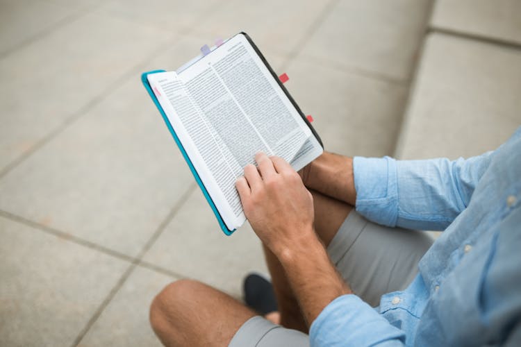 Person In Blue Long Sleeves And Gray Shorts Holding A Bible 