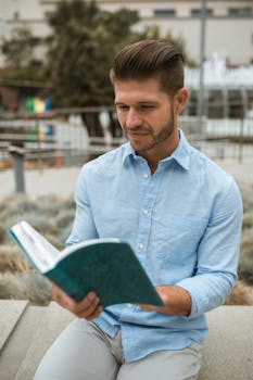 一个年轻人在阳光明媚的户外看书，他脸上长着毛发