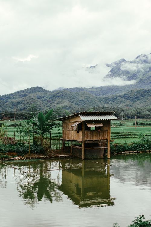 Free A serene view of a wooden cabin by a lake reflecting the nearby mountains and foliage. Stock Photo