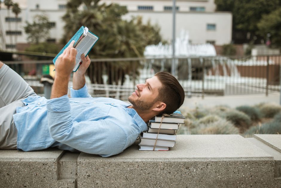 A man relaxes reading a book outdoors on a concrete bench, enjoying a sunny day. A man relaxes reading a book outdoors on a concrete bench, enjoying a sunny day.