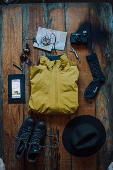 Flat lay of travel gear including jacket, shoes, camera, hat, and map on rustic wooden table.
