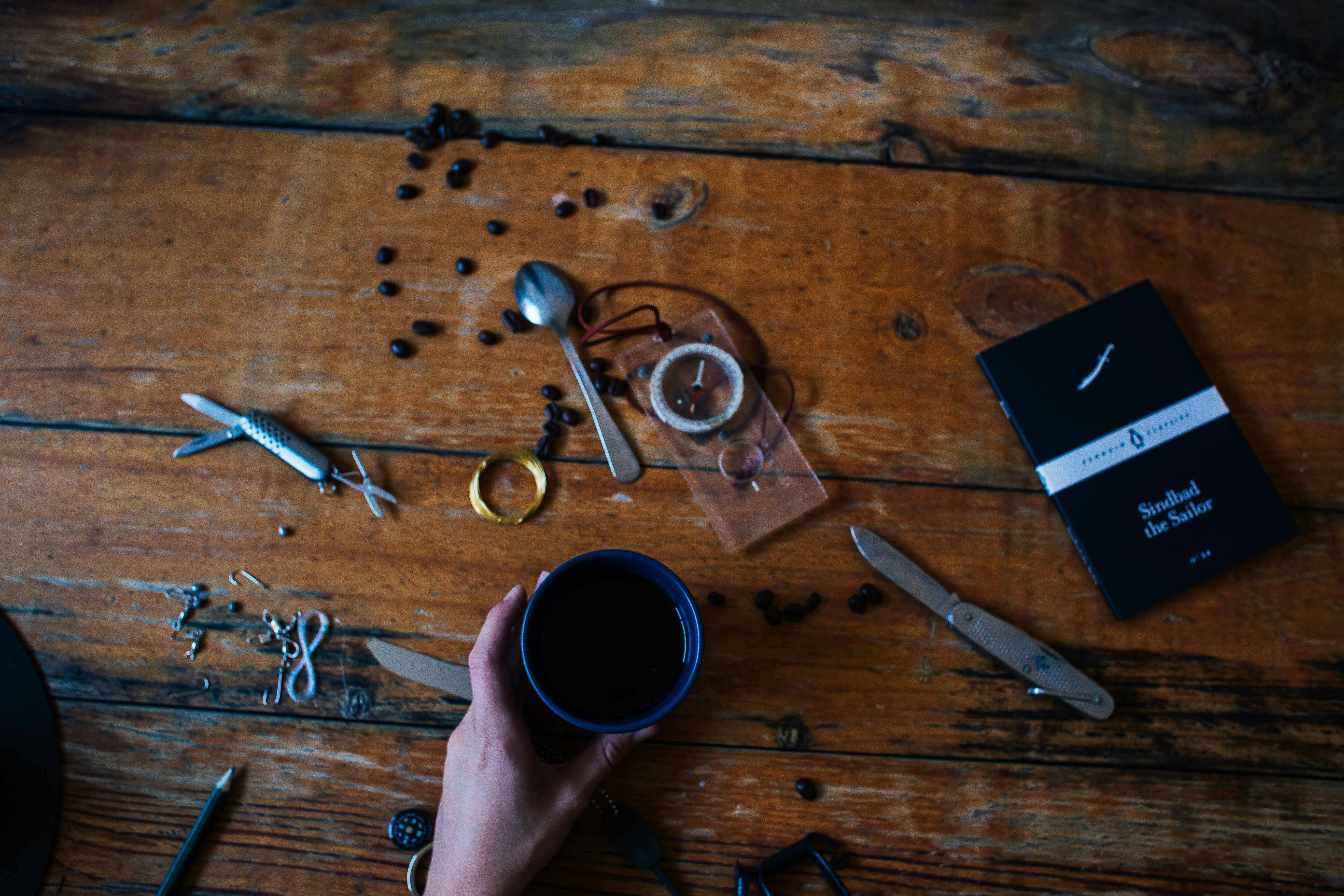 An artistic composition featuring a coffee cup, tools, and a book on a rustic wooden table.