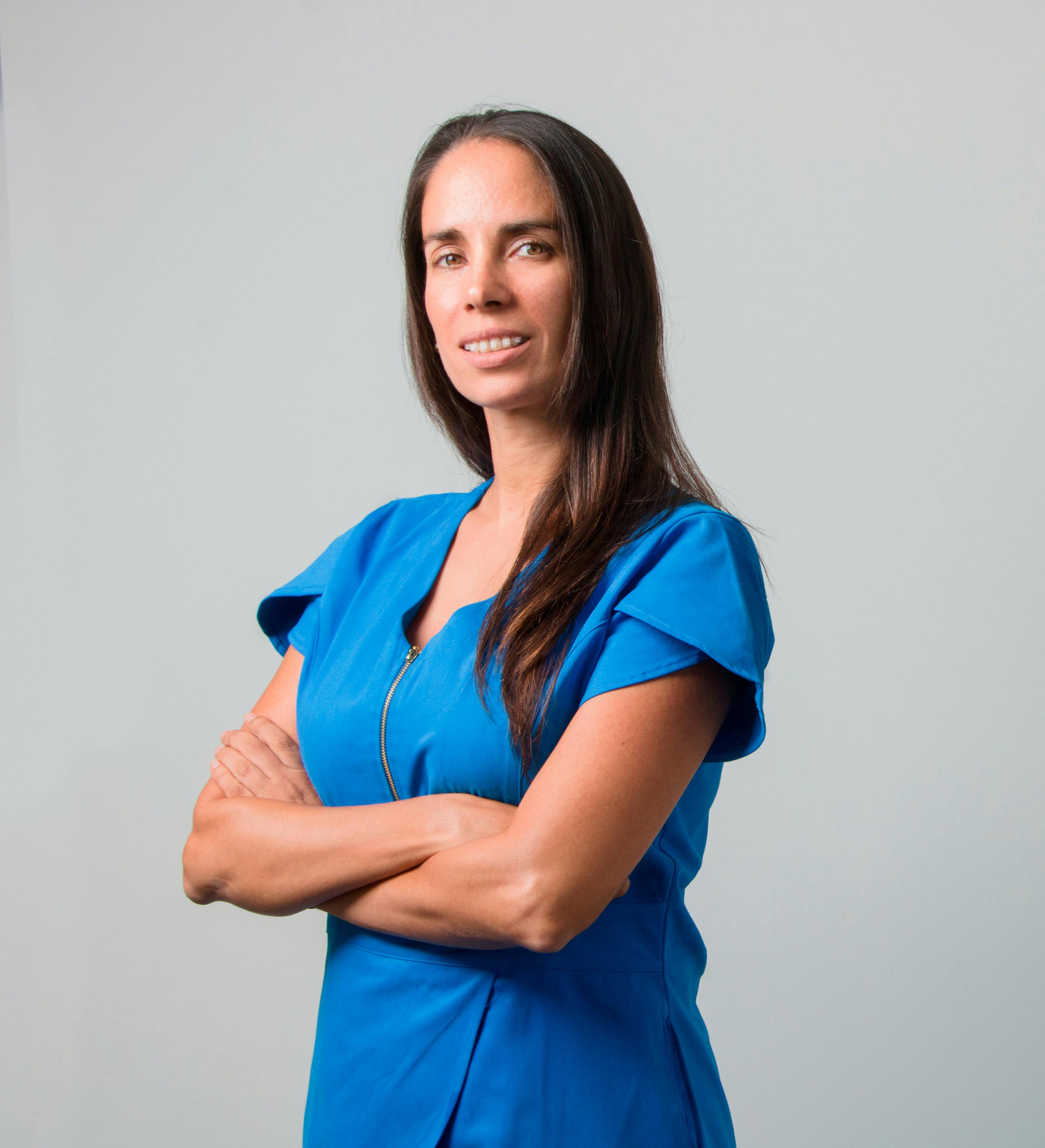 Portrait of a confident woman with arms crossed in a vibrant blue dress against a neutral background.