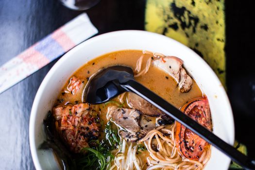 High-angle view of pork ramen with vegetables and sesame seeds in a white bowl.