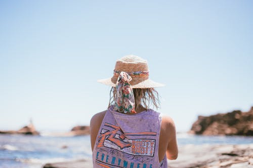 Free Woman in Blue Tank Top Wearing Brown Straw Hat Standing on Beach Stock Photo