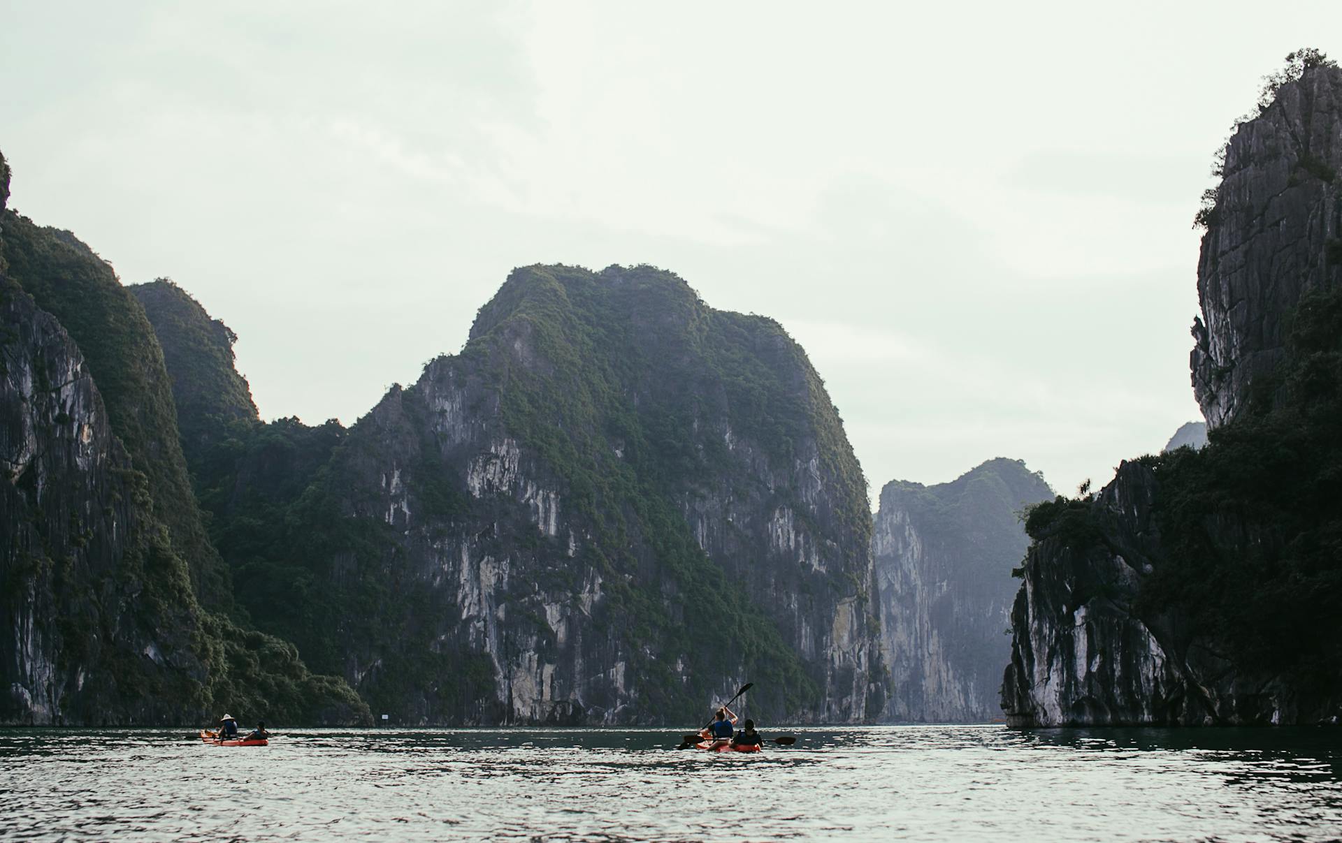 Two kayakers paddle between towering limestone cliffs on a tranquil waterway, perfect for outdoor adventure.