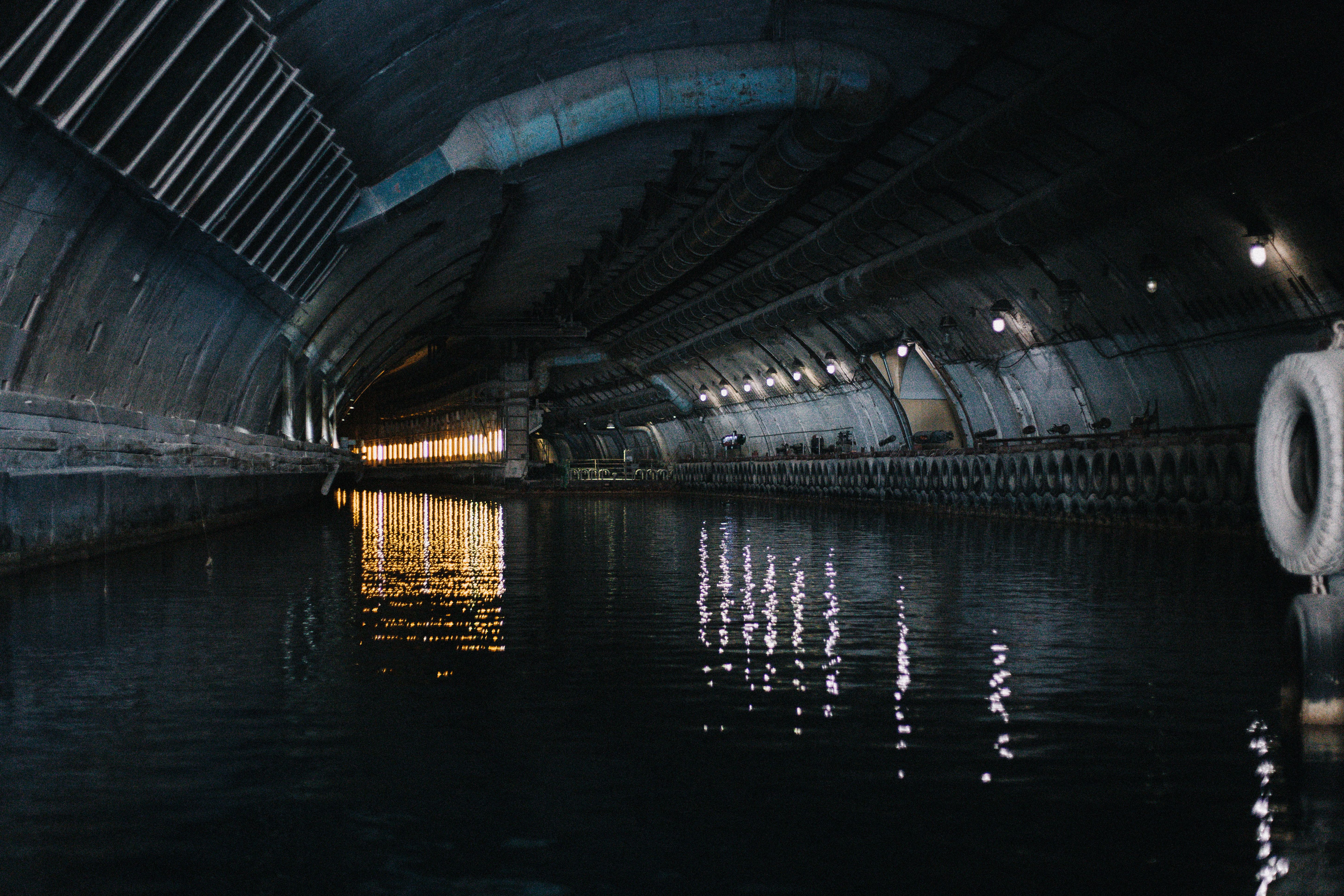 Explore the mysterious atmosphere in this dimly lit underground canal tunnel with captivating reflections on water.