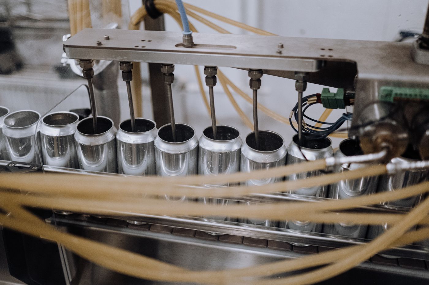 Open aluminum cans aligned beneath filling nozzles, with guide rails and tubing around the station