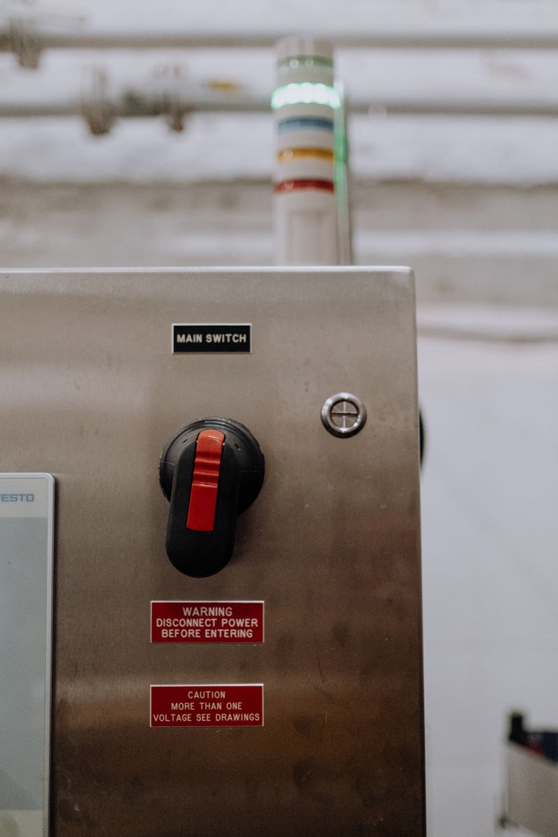 Stainless steel industrial main switch with safety warnings.
