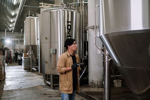 在一家啤酒厂，亚洲人正在检查不锈钢罐，展示现代工业流程