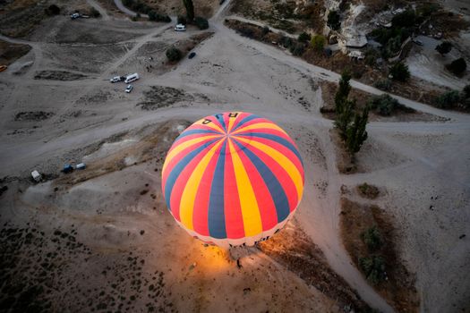 Vibrant hot air balloon from above illuminates desert landscape with colorful stripes.