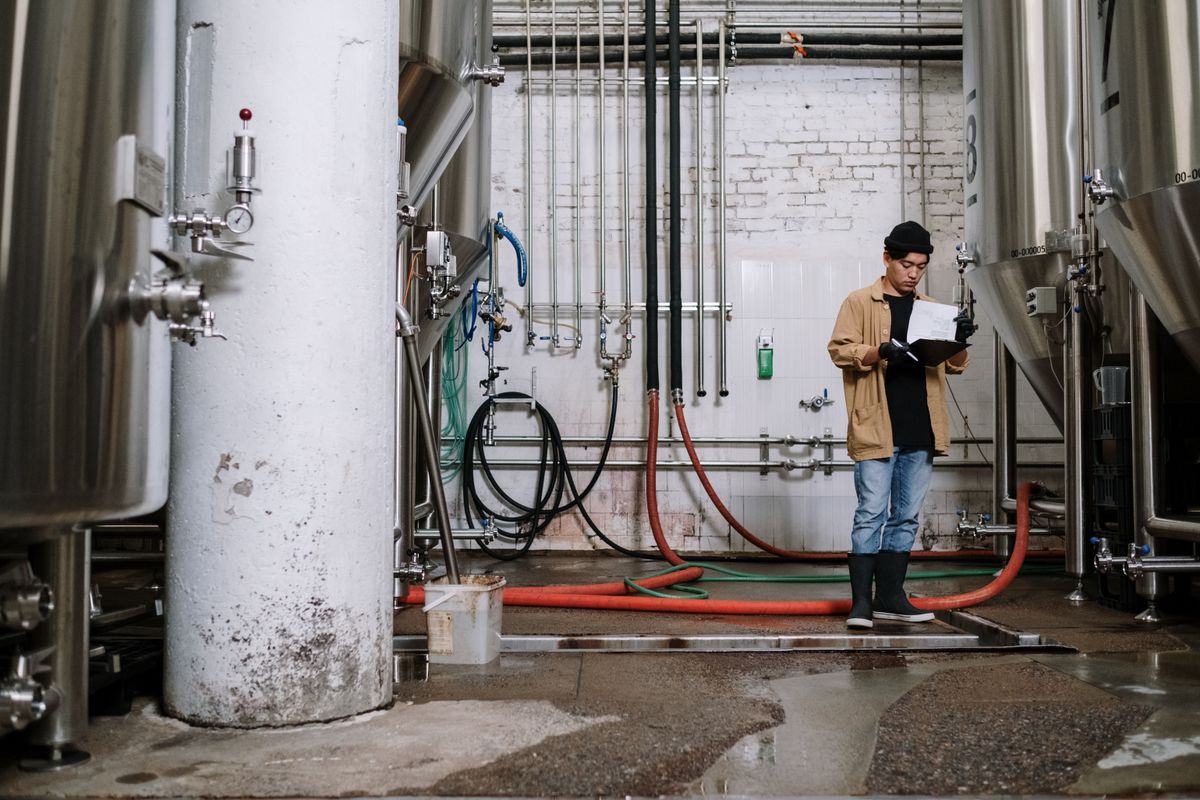 A production supervisor reading a batch record document beside process tanks in a manufacturing plant
