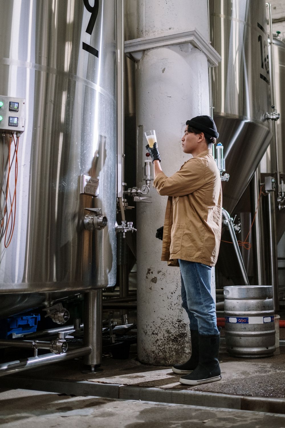 Brewer checking a fresh pour beside the stainless fermenters